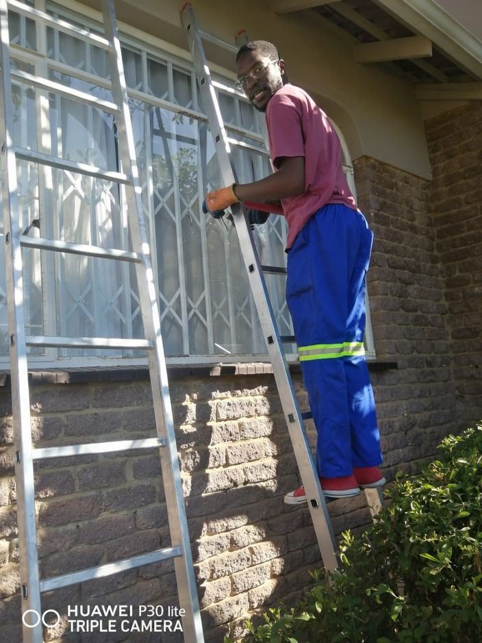 A fitter on a ladder working on a window behind a security gate