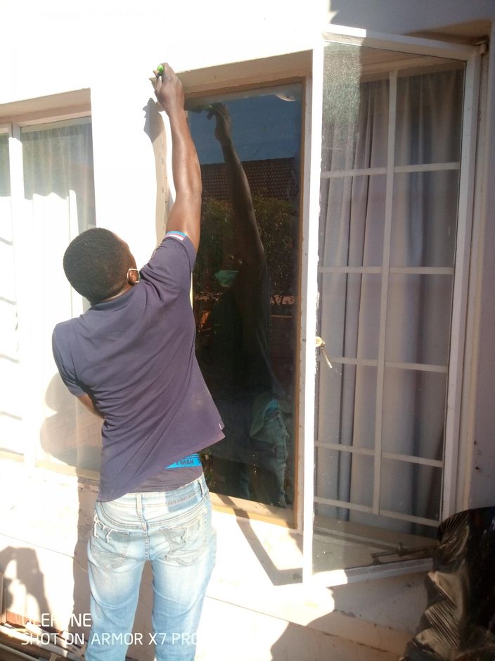 A fitter working on a window frame beside a burglar gate