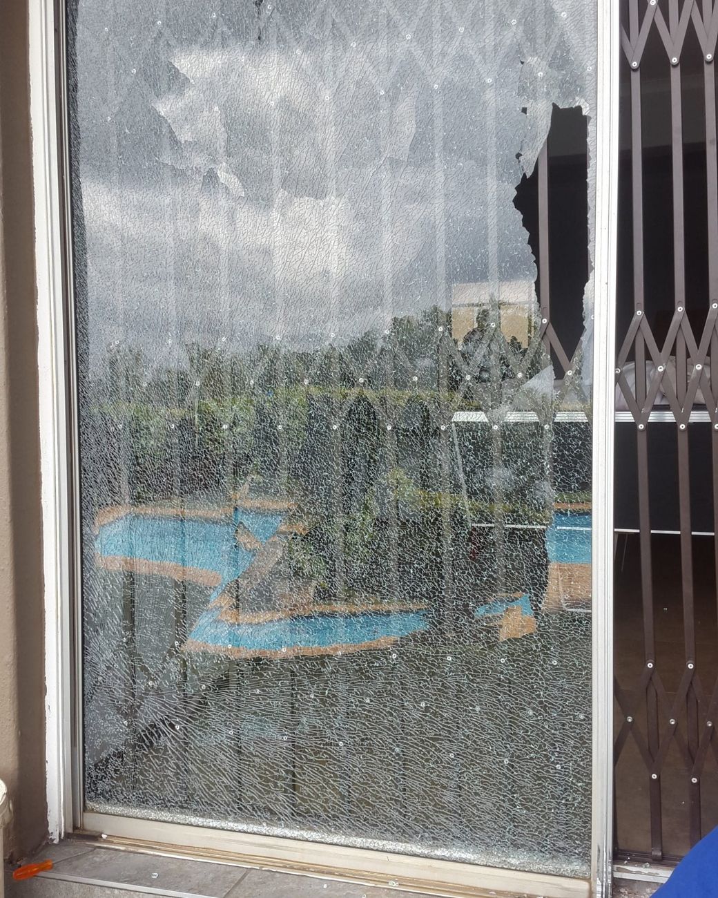 A sliding door with a large broken pane beside a security gate