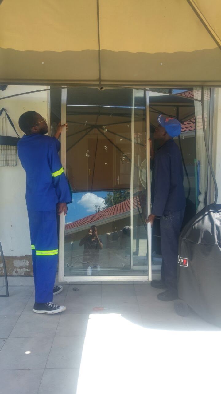 Two fitters working on an aluminium sliding door on a covered patio