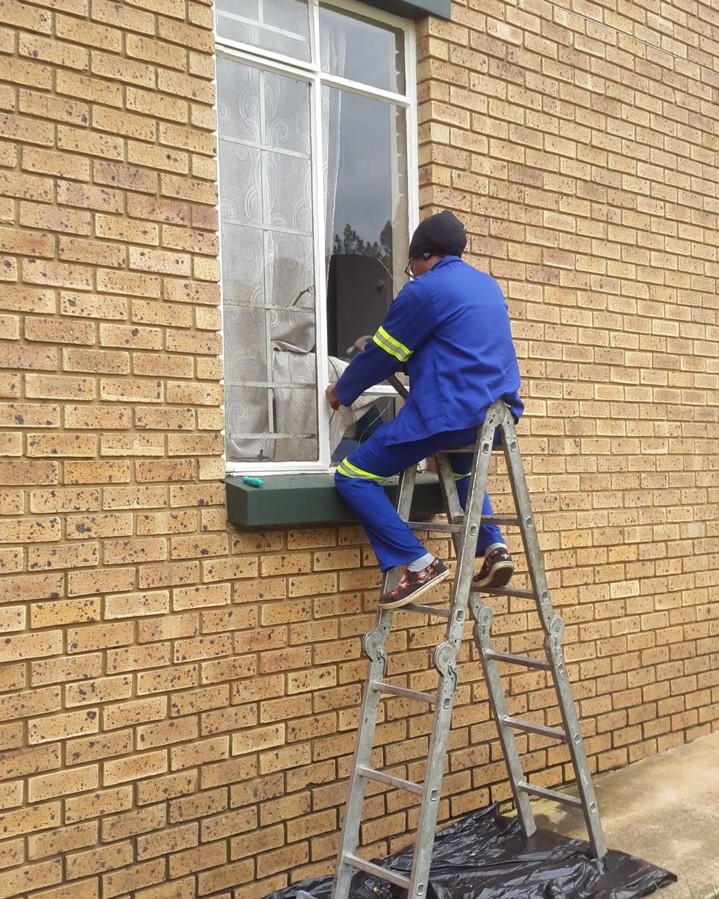 A fitter on a ladder working on a window in a face-brick wall